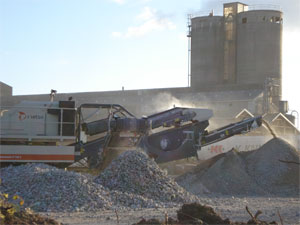 Billedet viser en gravemaskine der graver i betondynger p en byggeplads
