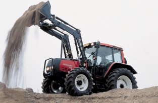 Traktor der graver grus med frontl�sser p� kant af grusgrav