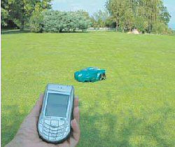 Robotplæneklipper på en græsplæne og en hånd med en mobiltelefon i