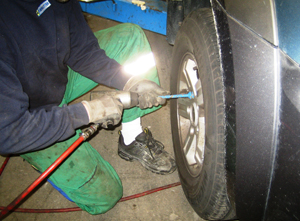 En mand skifter dæk på en bil med et værktøj i hånden