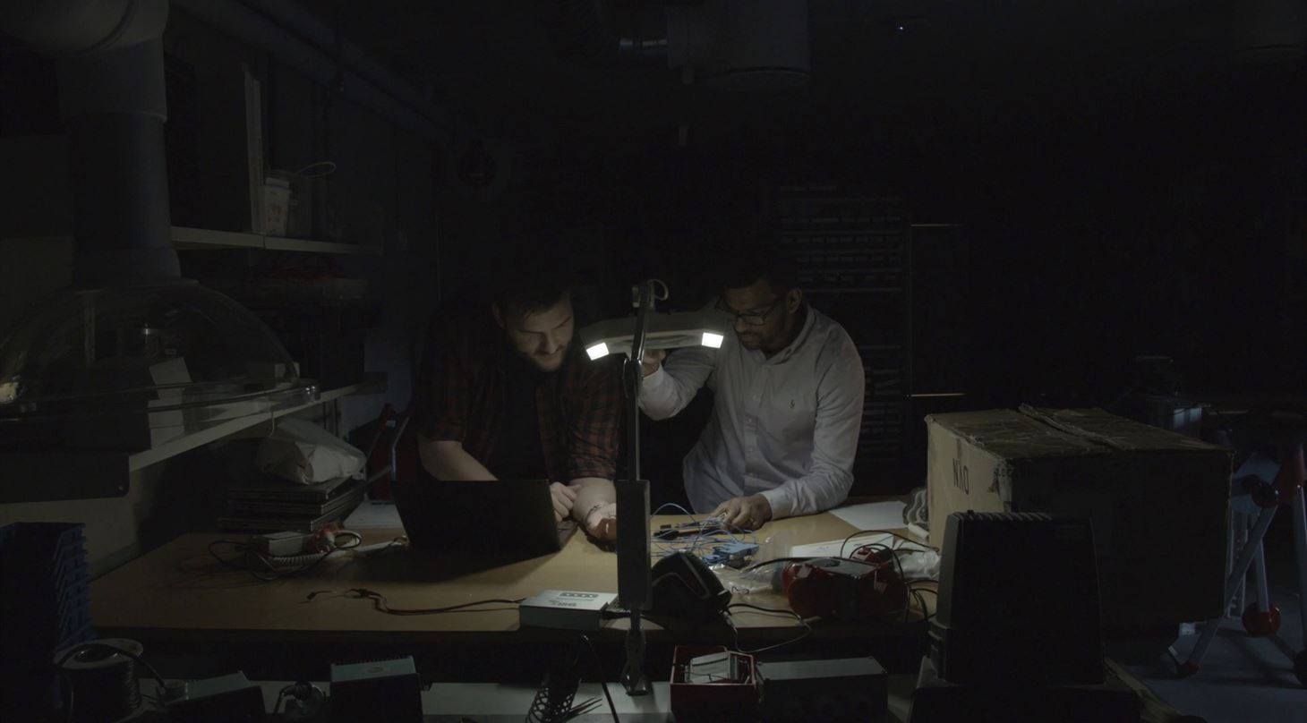 to mænd sidder i mørket med en lampe og arbejder med elektronik