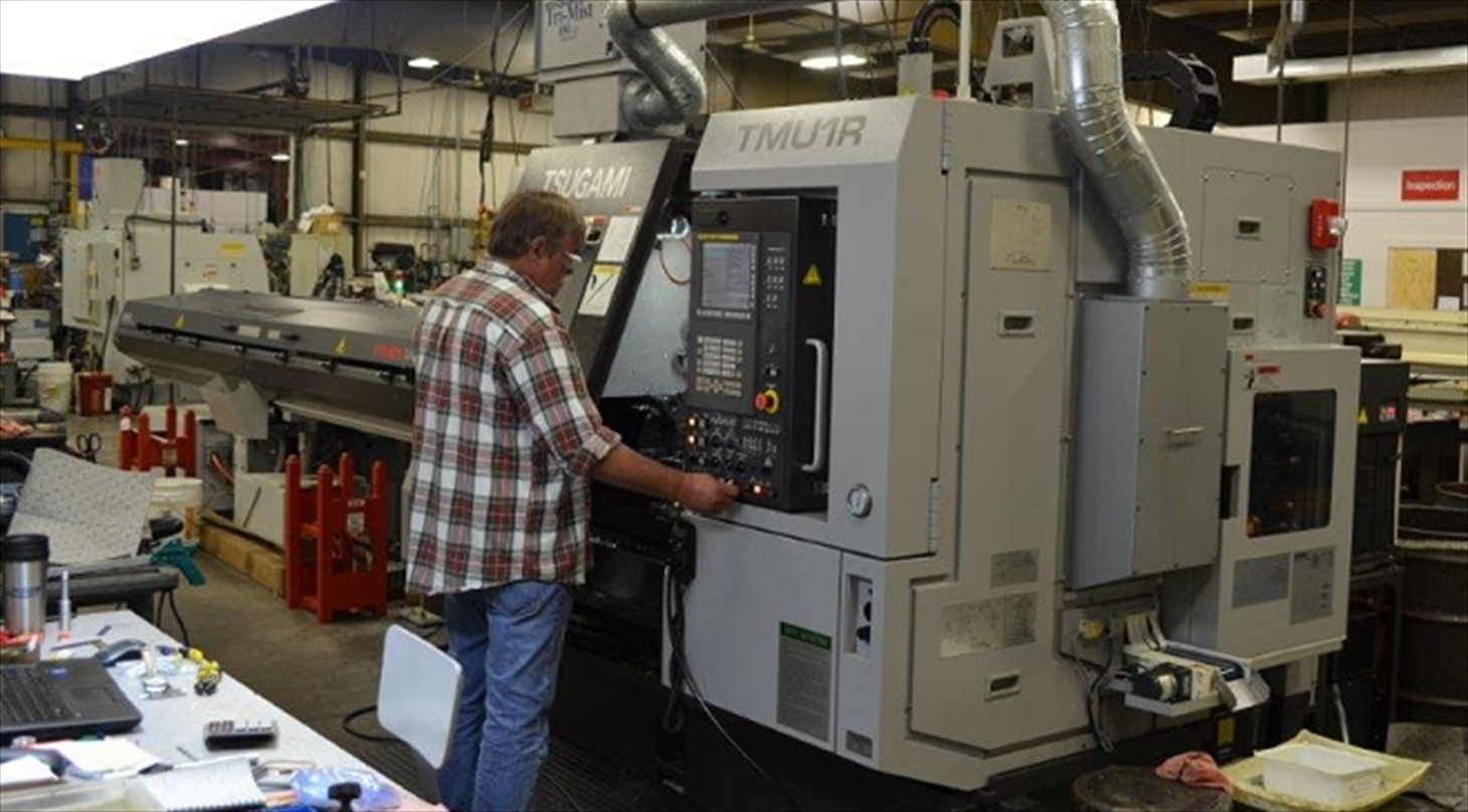 Billede af en mand, som står ved en stor computerstyret industrimaskine.