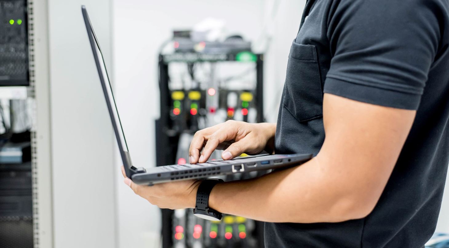Mand står med laptop og teknologi i baggrunden