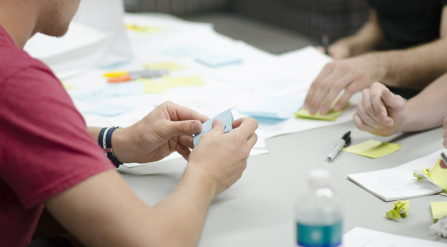 Skrivebord med post-its og delvis synlige personer