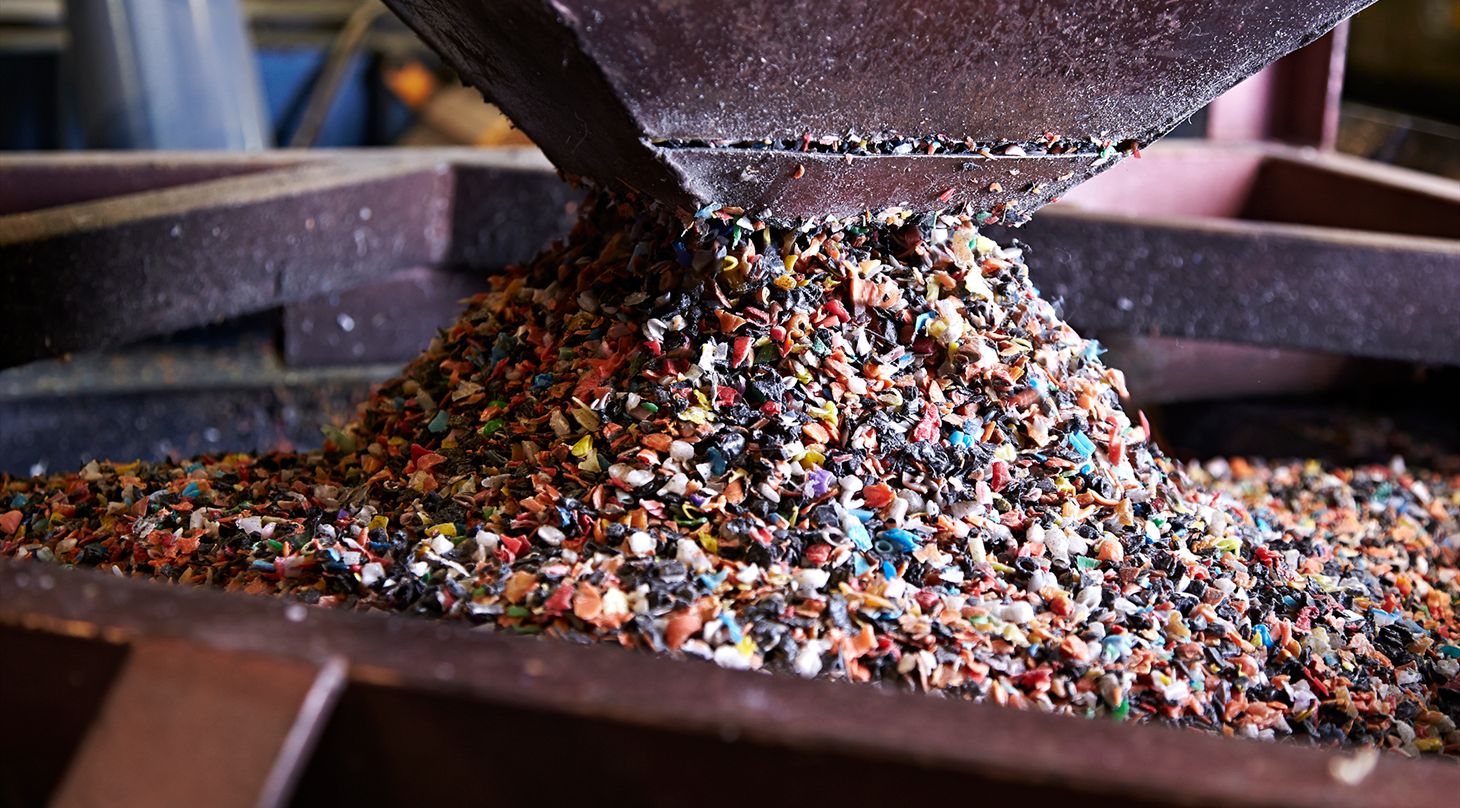 Billedet viser et close-up af granuleret plast, der kommer ud af en stor tragt og ned i en beholder.