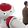 Et billede af robotten Nao med to mennesker i baggrunden.
