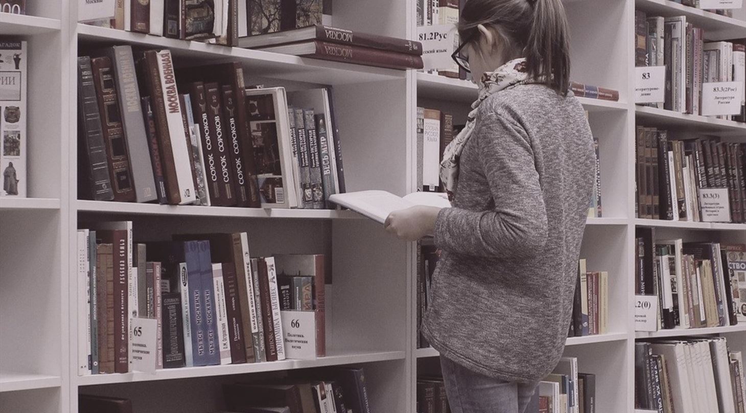 Et billede af en person, der str og kigger i en bog p et bibliotek.