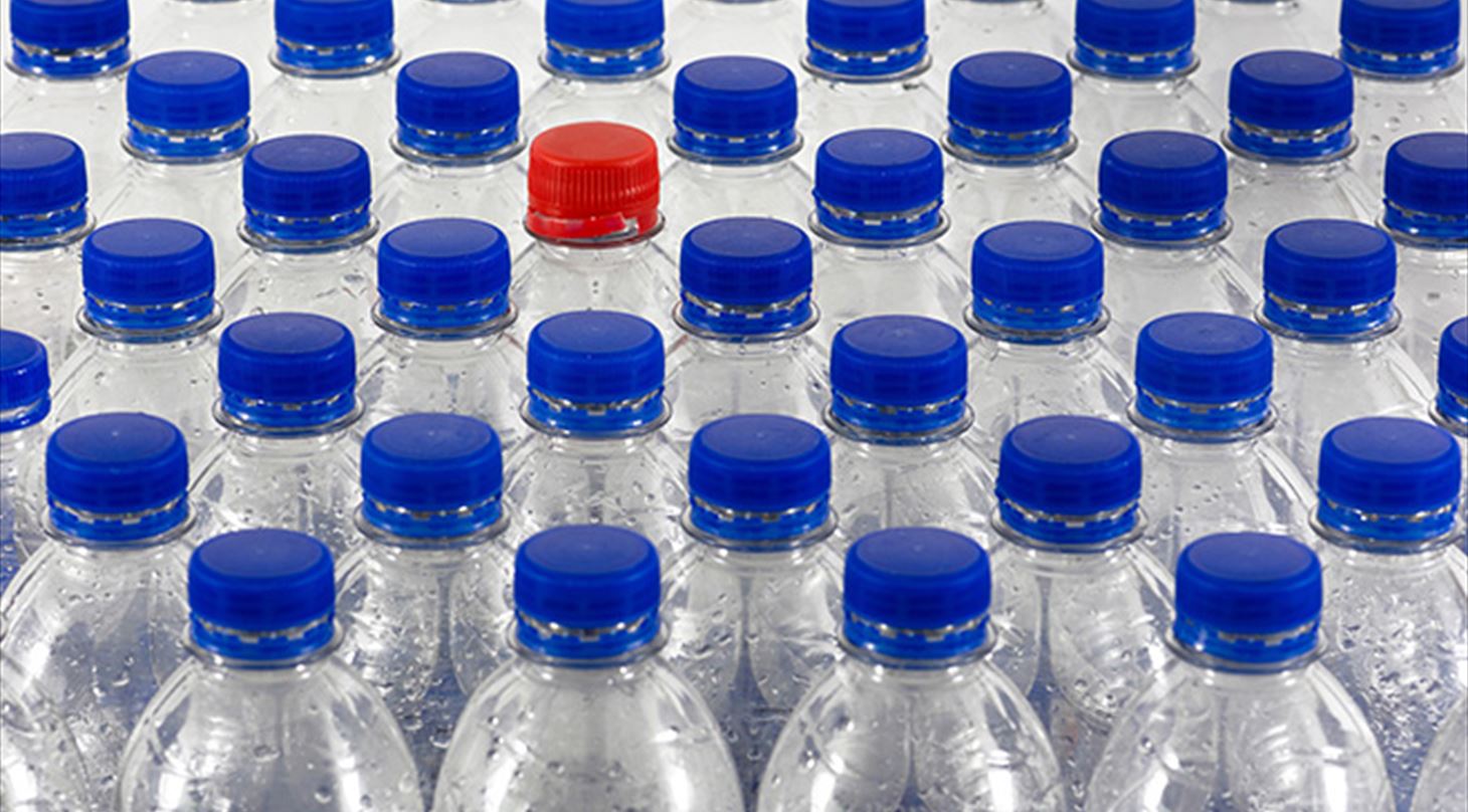 Billedet viser en masse plastflasker opstillet i en samlet klynge, størstedelen af flaskerne har blå låg undtagen en enkelt som har rødt låg. Billedet er brugt til lederen i Medlemsinformation nr. 5-19