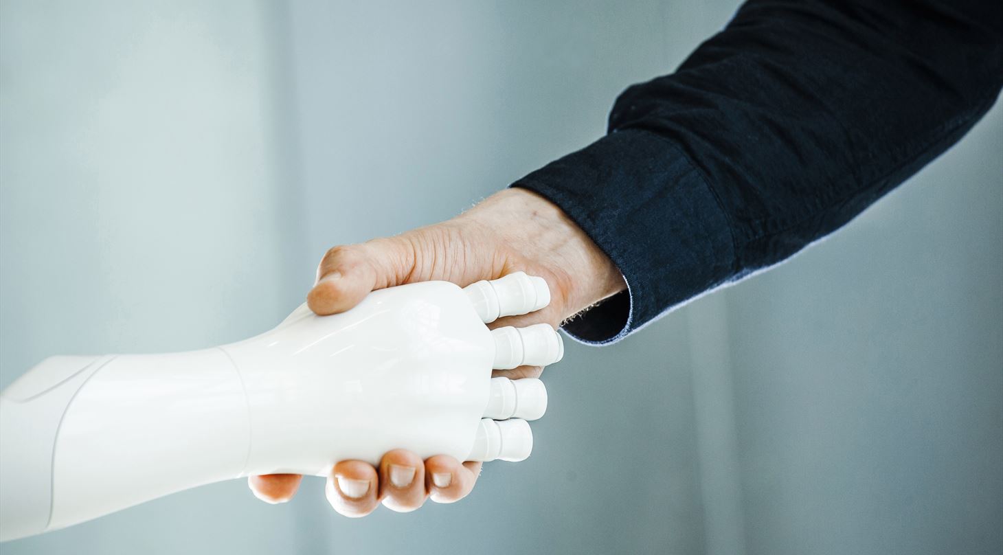 En menneskelig hånd og en robothånd giver et håndtryk.