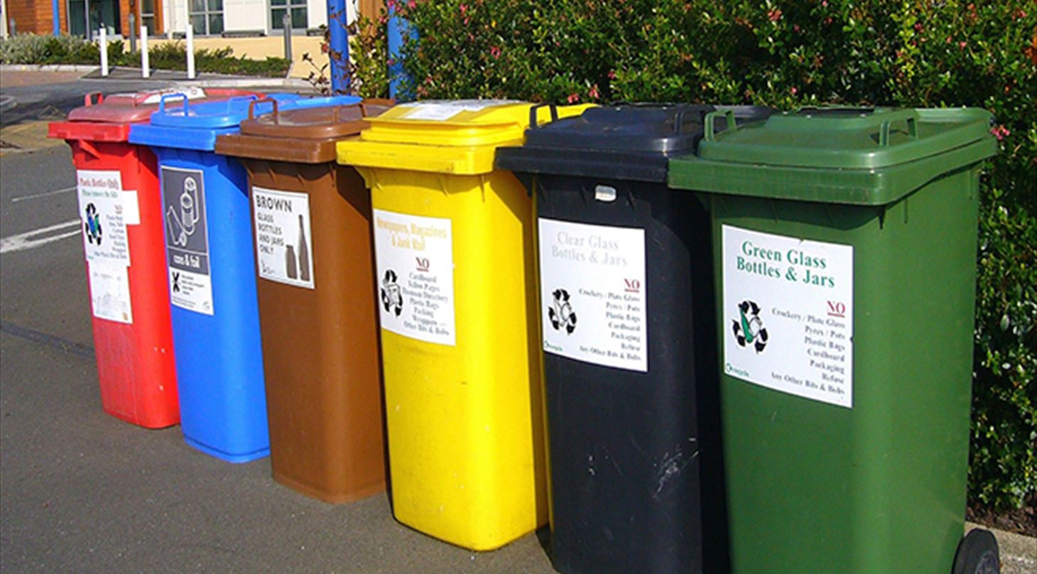 Billedet viser seks forskellige indsamlingscontainere til affald til genbrug, containerne er i farverne grøn, blå, gul, brun, mellemblå og rød