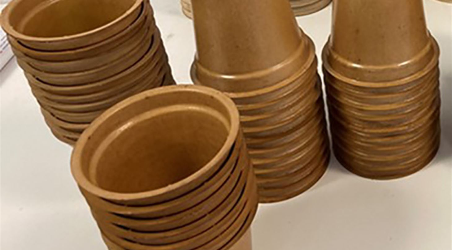 Billedet viser et antal bæredygtige plastfrie papiremballager - et bæger - udviklet i projektet Bæredygtige plastfrie papiremballager til syrnede mælkeprodukter". Billedet er brugt til en artikel i Plast og Emballages Medlemsinformation nr. 1-2022