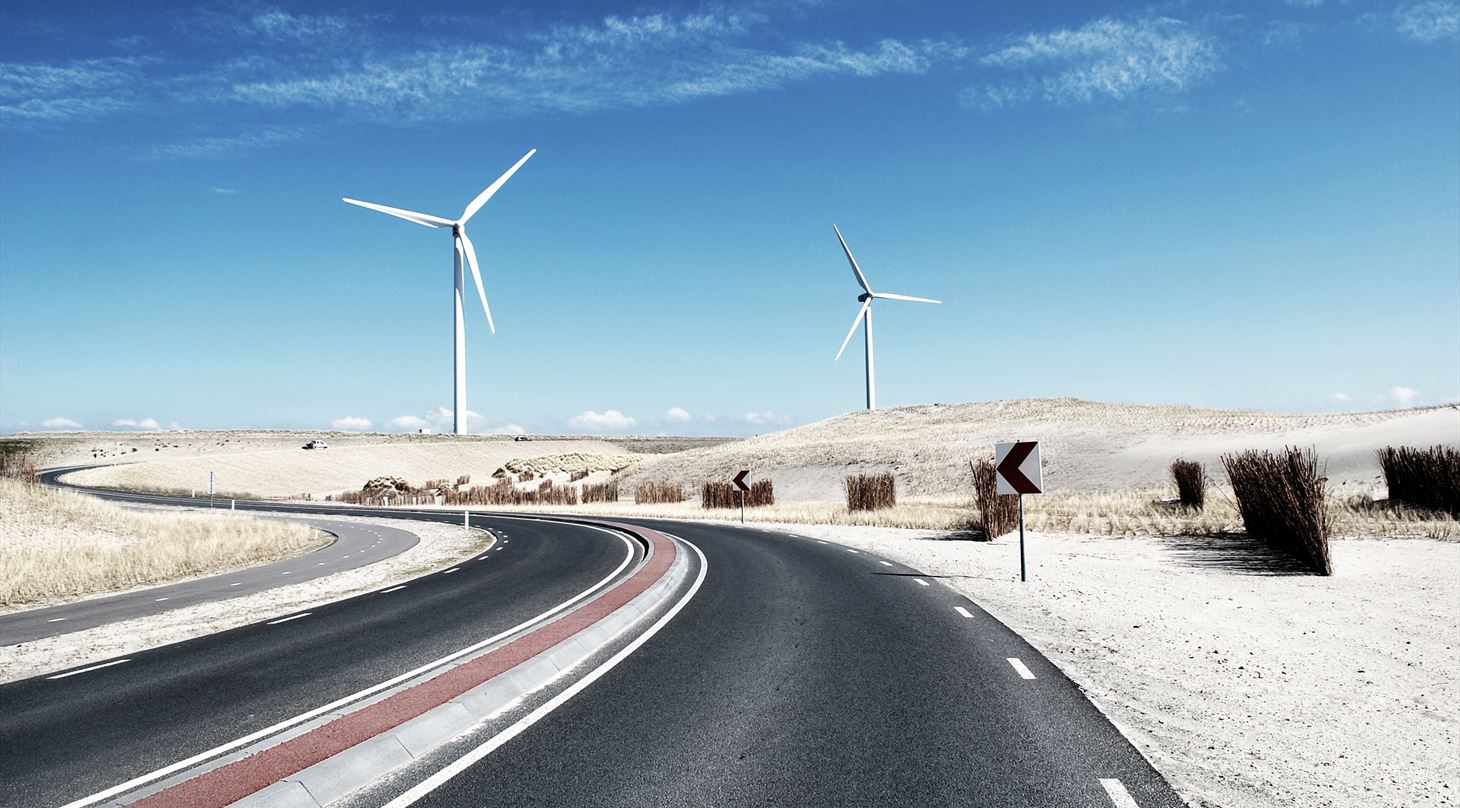 En motorvej i en ørken med vindmølle i baggrunden