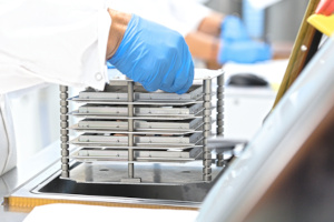 Laboratorie, medarbejder med handsker tager en kurv op fra maskine