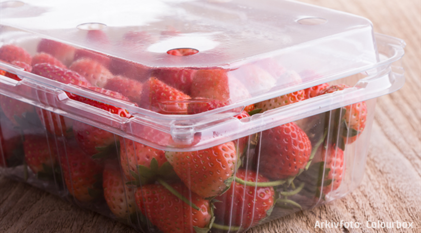 Billedet viser friske jordbær i en gennemsigtig plastboks som står på et træbord. Billedet er arkivfoto fra Colourbox