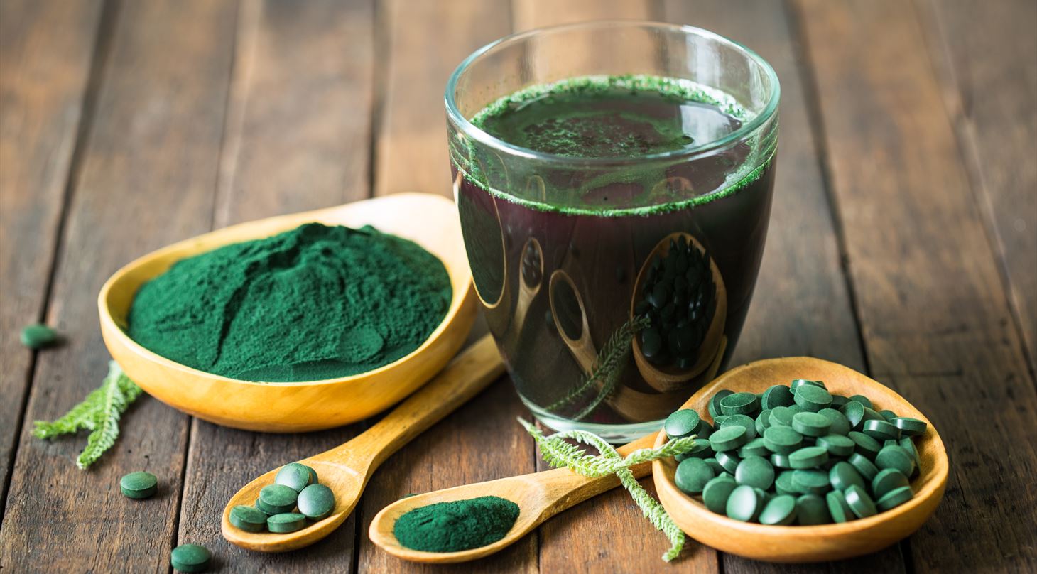 Billeder af grnbl spirulina-alge pulver i et glas p et trbord