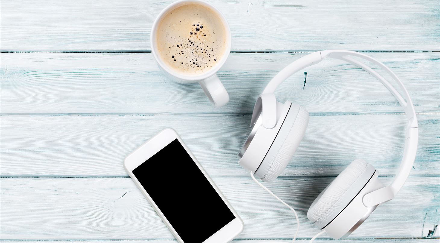 Et bord med høretelefoner, en telefon og en kop kaffe