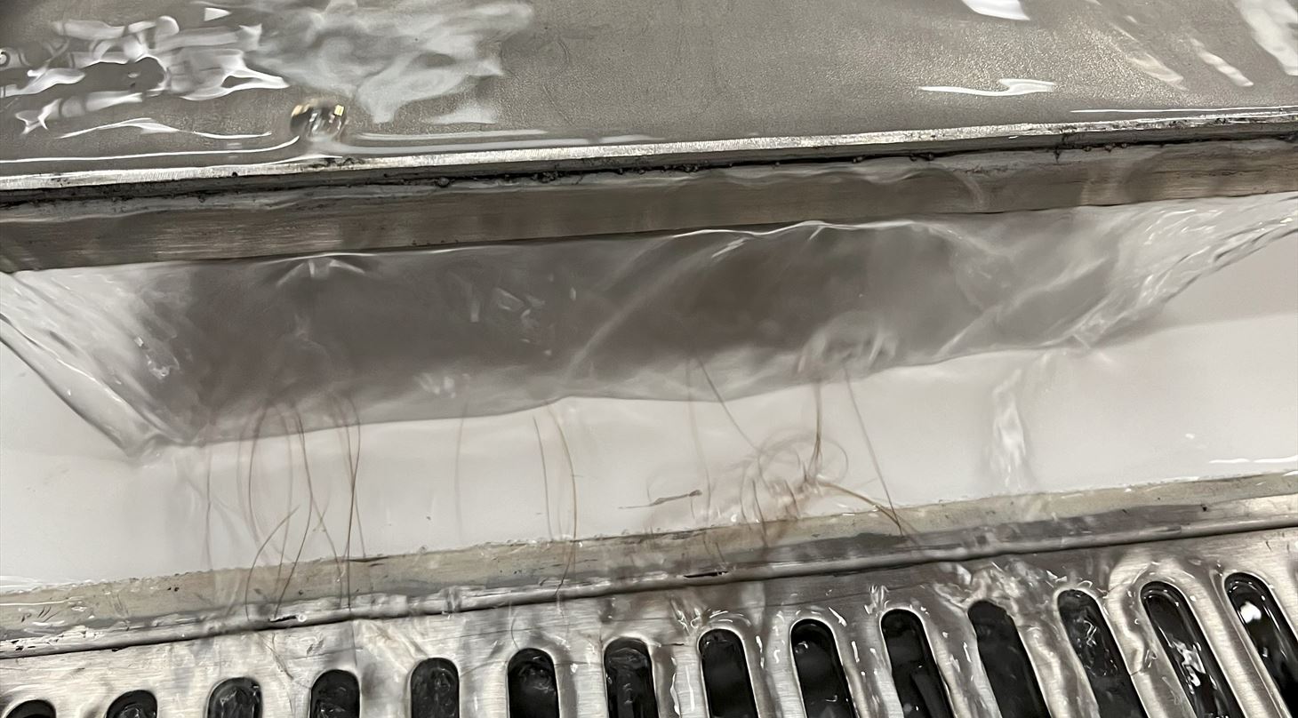 Billedet viser vand l�be hen over en metalplade og ned i en afl�bsrende. Vandet er tilsat h�rfibre for at simulere en tilstopning. 