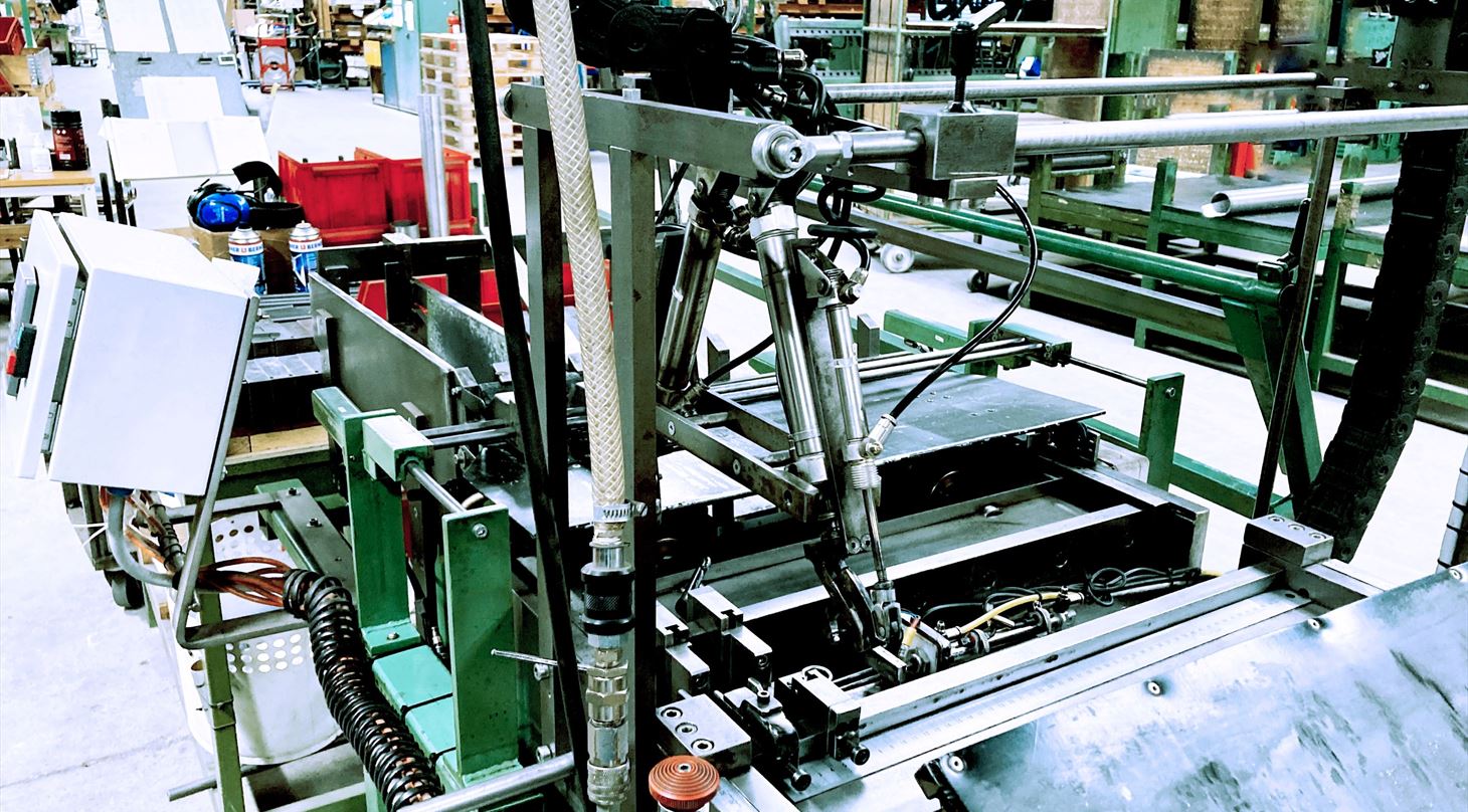 Industriel produktionsmaskine med hydrauliske komponenter og styresystemer i en fabrikshallen med lagerhylder i baggrunden - illustrerer avanceret produktionsudstyr og automation