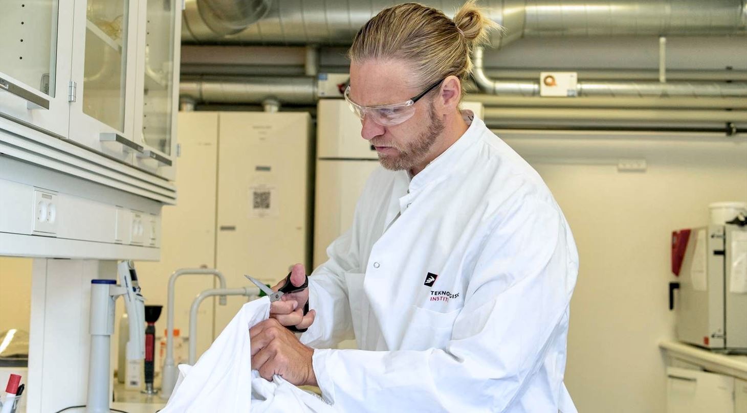 Mandlig forsker klipper i hospitalstekstiler i et laboratorium
