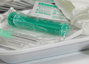 Billedet viser en hvid papirbakke, hvori der ligger forskellige medicinske produkter bl.a. en gr�n spr�jte, vaskeservietter og andre ting pakket i plastfolier.
